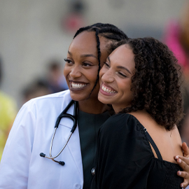 female student in white coat smiling and hugging another female