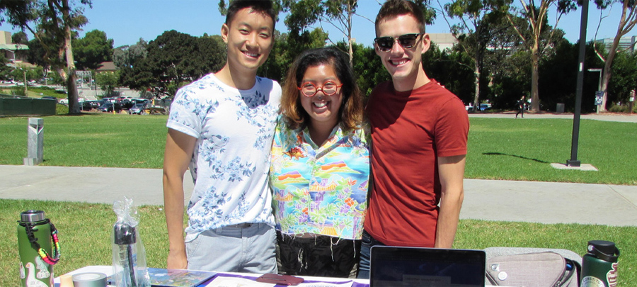 Two male and one female student standing together smiling in an outdoor courtyard.