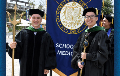 photo of two men wearing graduation regalia holding a School of Banner banner and a trident