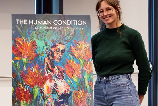 Female student standing next to large image of The Human Condition magazine cover artwork