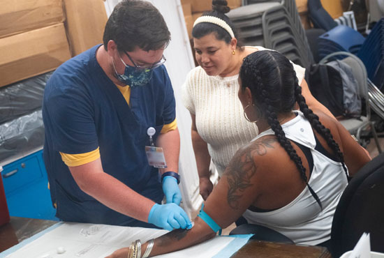 medical student preparing to draw blood on patient with physician watching in background