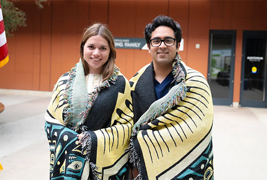 Male and Female student standing with blankets around their shoulders