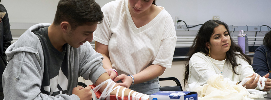 6 of 6, Female high school student practicing putting a splint on the left arm of a male student