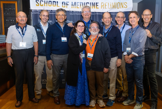 Group of School of Medicine Alumni smiling  while standing under a School of Medicine Reunion banner