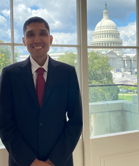 Alexander Tenorio smiling by a window with the US Capital building in the background