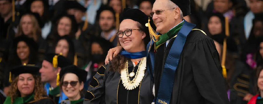 12 of 13, side view of female student and male professor in graduation regalia smiling