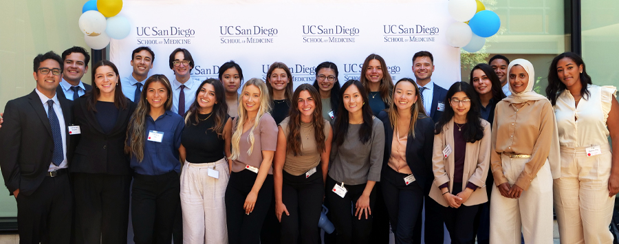 3 of 7, Students smiling in front of School of Medicine branded background