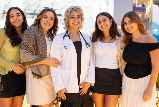 female student wearing white coat surrounded my female family/friends