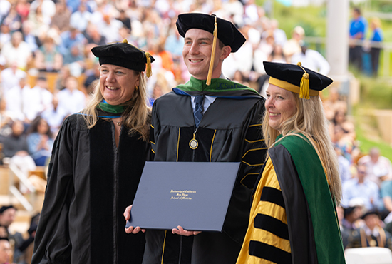 student in commencement regalia flanked by deans on left and right