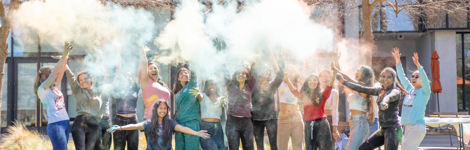 Group of female students celebrating Holi, the Hindu Festival of colours by tossing colored chalk dust into the air.