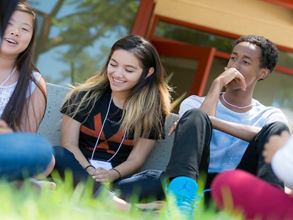 three students sitting in grass smiling
