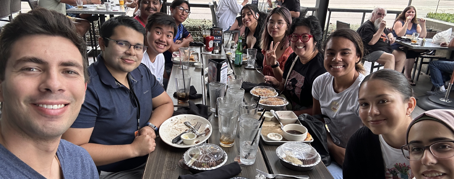 5 of 6, selfie of large group of people eating a meal at a long table smiling at camera